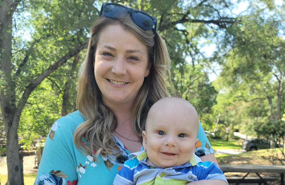 Smiling baby being held by his Mom in a greenish blue shirt.