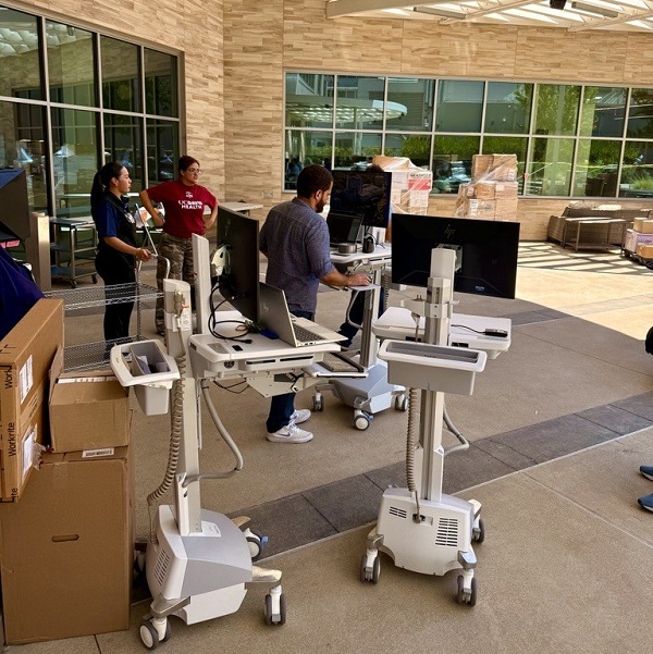 Workstations with computers and medical equipment are set up outdoors, near boxes of supplies, as staff monitors the distribution.