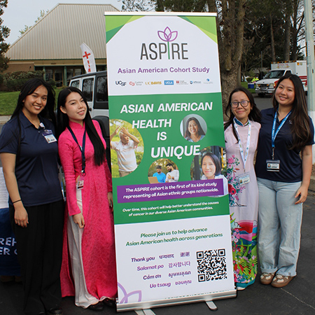 Four women standing next to a vertical banner with a green background that reads “ASPIRE Cohort” and contain information including a QR code about how to participate.
