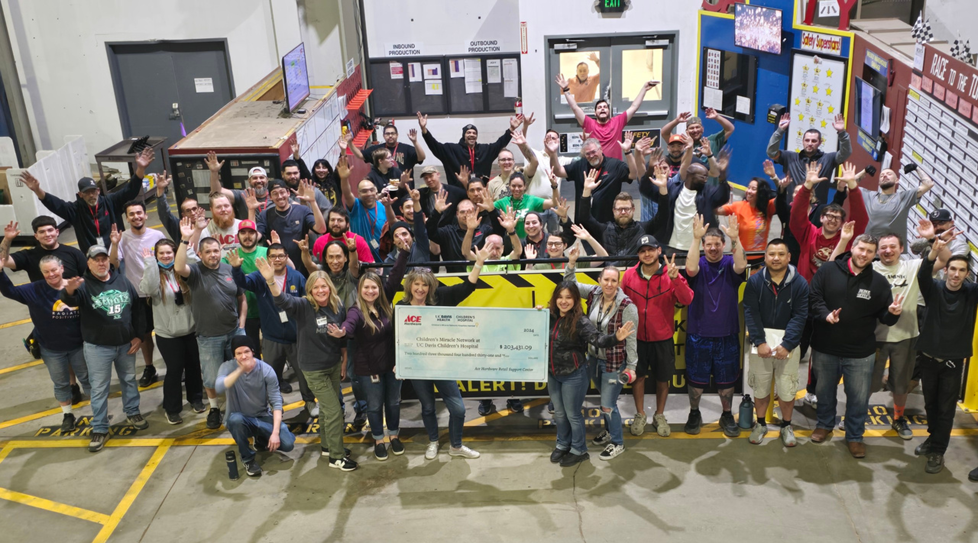A photo taken from a high angle showing dozens of people, with the ones in front holding an oversized check from ACE