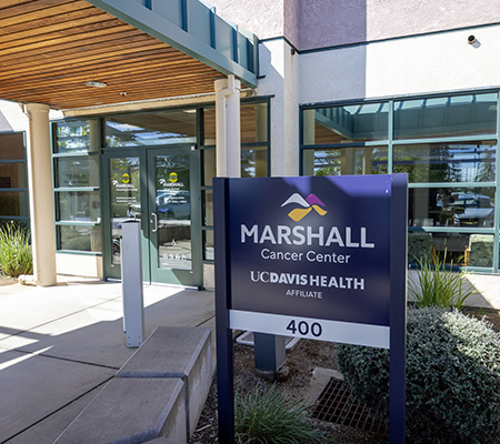 Exterior of building with glass doors and sign in the foreground that reads,  “Marshall Cancer Center, UC Davis Health affiliate”