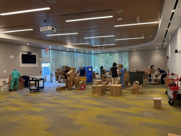 Large room with team members sorting and organizing boxes of medical supplies on tables and carts inside North Addition Office Building staging area