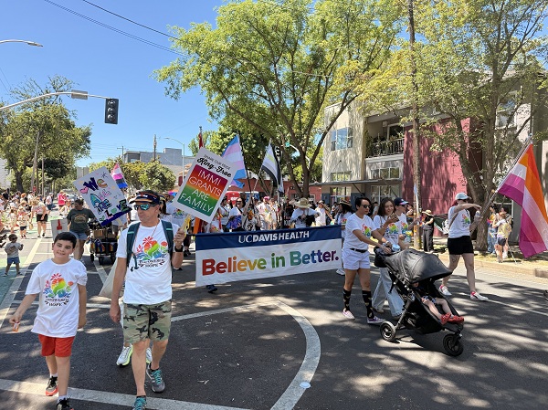 Group walking in a Pride parade holding a UC Davis Health banner, signs and pushing a stroller.