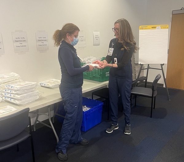 Two team members sorting medical supplies on a table with organized bins and stacked items in a distribution room at UC Davis Health