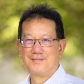 Headshot of a person wearing glasses, with short dark hair, smiling slightly against a blurred green background.