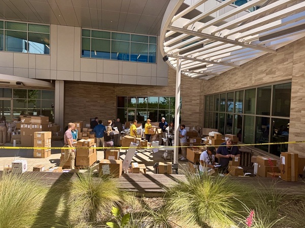 Group of people working among many boxes and pallets of supplies in an outdoor courtyard area while sorting and organizing items for distribution