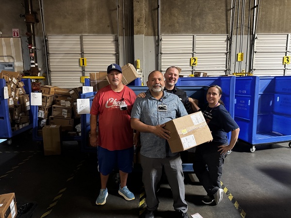Group of team members standing in front of bins of boxed medical supplies in a warehouse, while holding a package ready for distribution