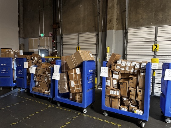 Large blue bins and pallets filled with boxes of medical supplies staged in a warehouse area for sorting and delivery