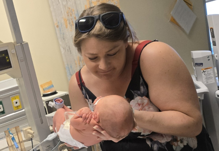 Woman holding baby in hospital, gazing down at her child.