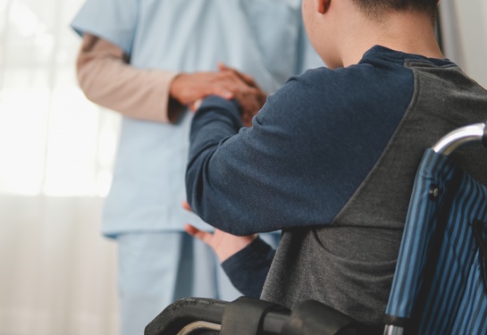 Boy in wheelchair faces someone wearing blue scrubs