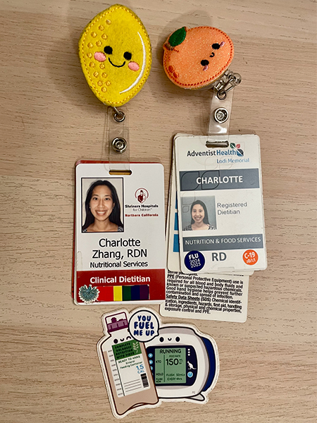 Two hospital ID badges from Charlotte Zhang’s dietitian career with cartoon fruit badge reels and healthcare-themed stickers 