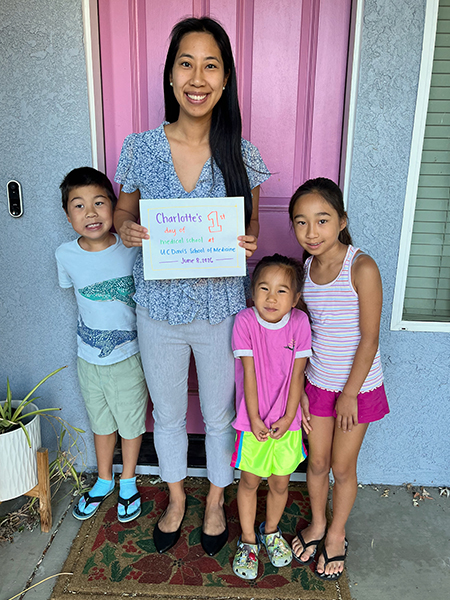Charlotte Zhang with her three children in front of a house, holding a sign stating her first day the UC Davis School of Medicine 
