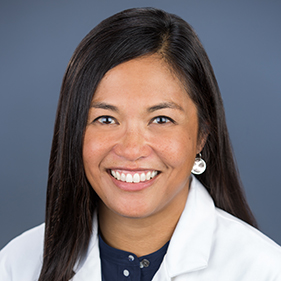 Headshot of smiling woman with dark hair wearing a white doctor coat