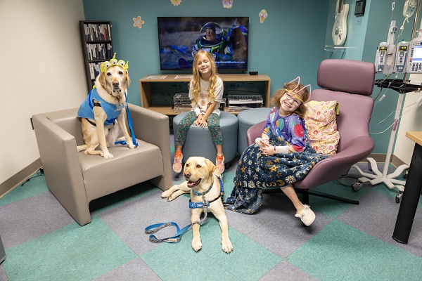 Two pediatric patients sit with two facility dogs in a hospital room at UC Davis Children's Hospital.