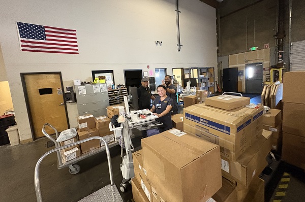 Employees work among boxes and carts inside a warehouse receiving area.