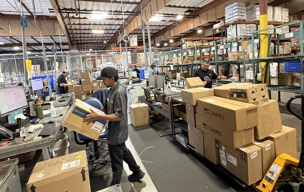 Employees work at warehouse stations surrounded by boxes, shelving and inventory racks.