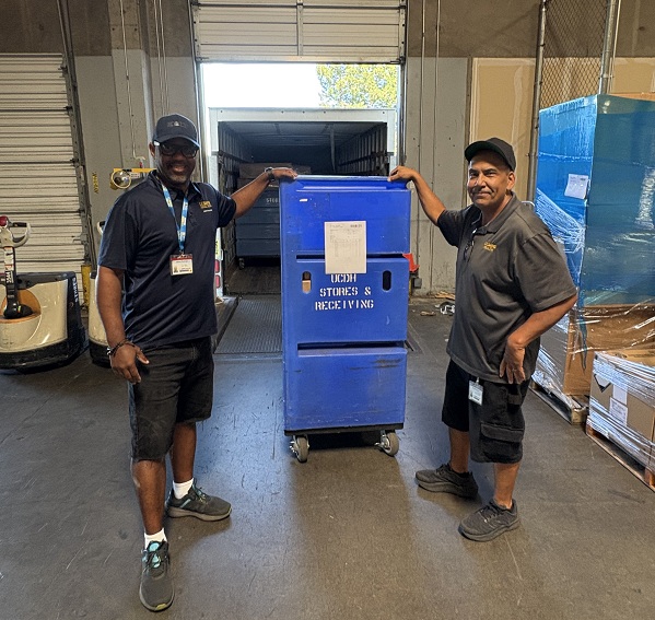 Two employees stand beside a blue rolling receiving container positioned near a loading dock.