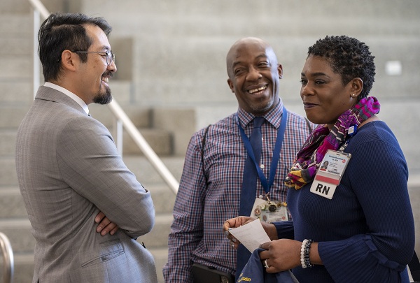 Three UC Davis Health employees talk in a building lobby while standing near a staircase.