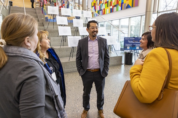 A group of people stand in a lobby and talk near a staircase decorated with banners and artwork.