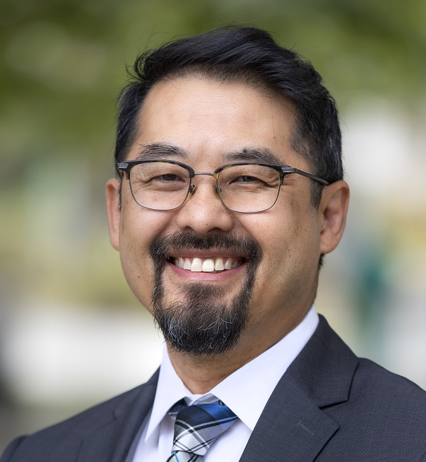 Portrait of Hendry Ton wearing glasses, a suit jacket and a patterned tie outdoors.