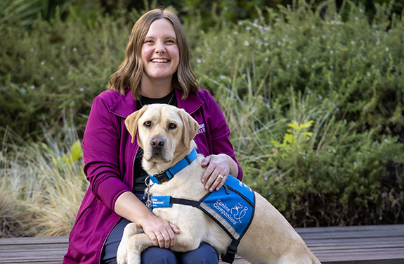 A person sits on a bench while a yellow labrador retriever rests his front paws on her lap