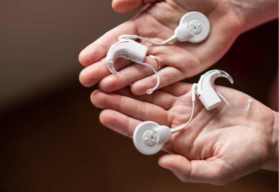Modern cochlear implant devices resting in open hands.