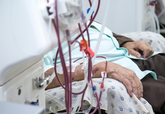 Patient undergoing dialysis is seated beside medical equipment in a healthcare facility.