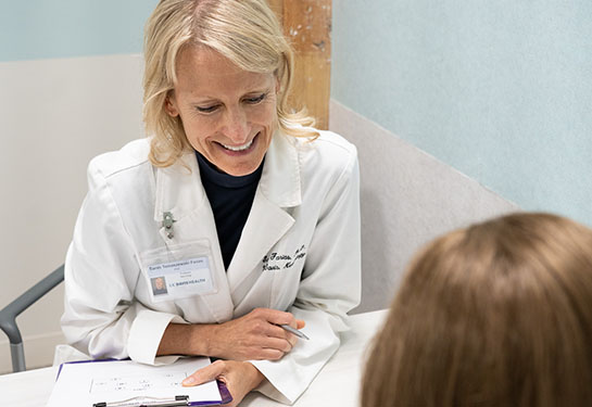 A researcher in a white coat talks with a patient at a table. 