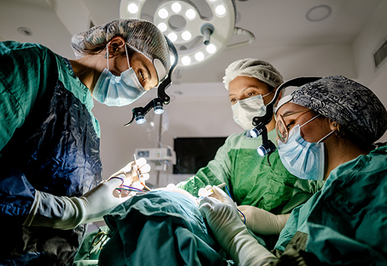 Three individuals on a surgical team work in an operating room.
