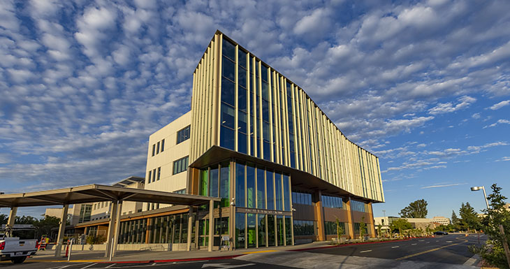A four-story building with a striking curved and angular design is shown against a blue sky with small white clouds. 