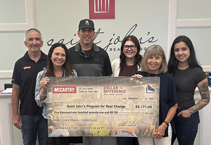 Six people pose with a $5,171 Dollar for Difference donation check benefiting Saint John’s Program for Real Change.