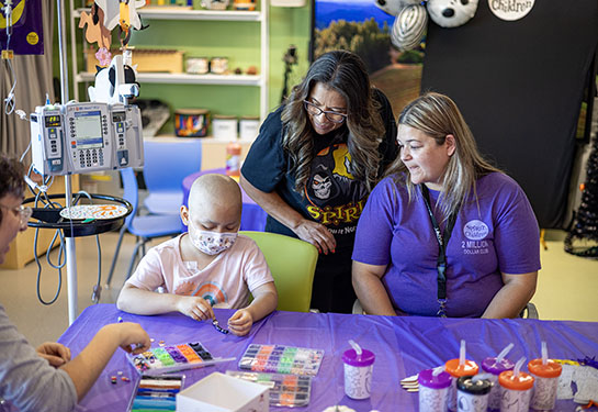 A child works on an art project with two people sitting at the table.