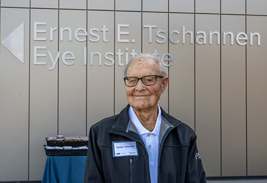 Ernest E. Tschannen, a smiling older man, stands in front of a building that bears his name.