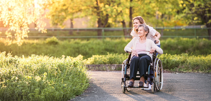young woman pushing older woman in wheelchair through a park