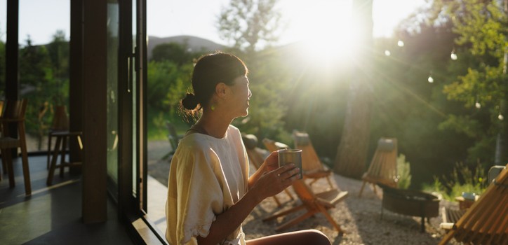 A woman holding a mug while looking at a sunrise. 