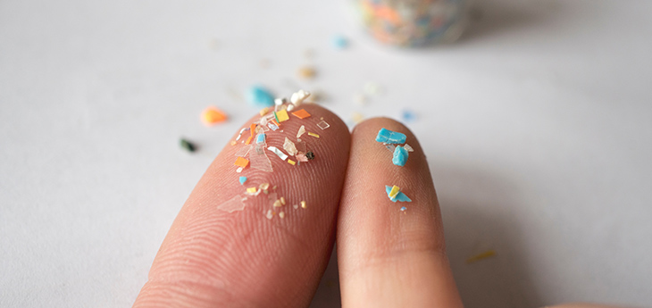 Close-up photo of microplastic pieces resting on the tips of two fingers.