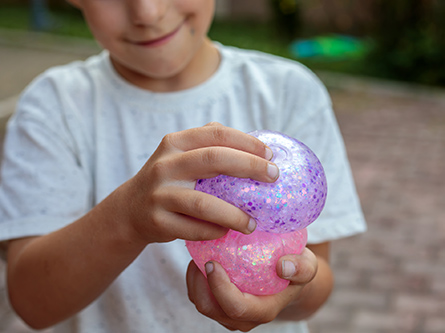 A young boy plays with a purple and pink, glittery squishy toy.