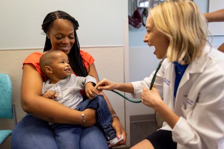Pediatric patient and their mother smile at a pediatric primary care provider.
