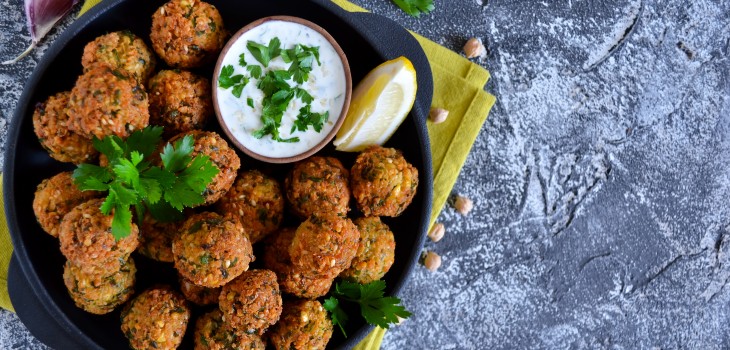 A bowl of greens and falafel drizzled with tzatziki sauce