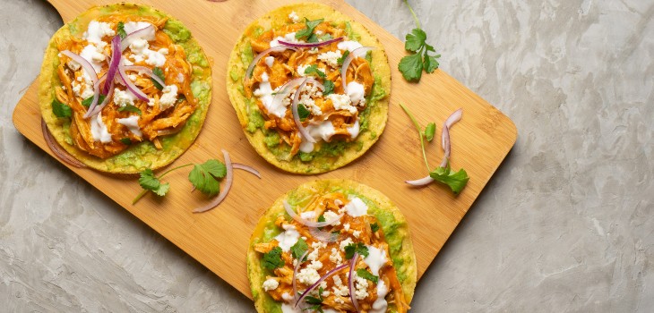 Three buffalo chicken tostadas on a wooden board