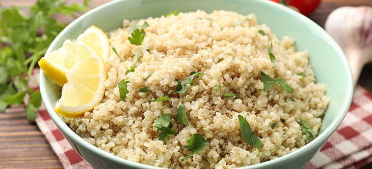 Bowl of quinoa with lemon slices, parsley, and garlic on wood table
