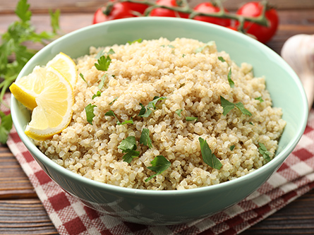 Bowl of quinoa with lemon slices, parsley, and garlic on wood table