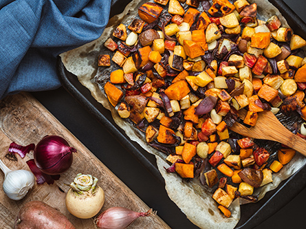 Colorful roasted root vegetables on a baking sheet with a wooden serving spoon