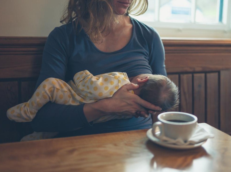 baby breastfeeding at table with coffee cup