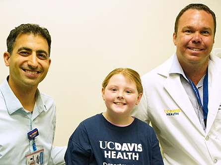 From left to right, Dr. Cameron Sadegh, Emily Roberts and Dr. Rick Price sit on an exam room bed.