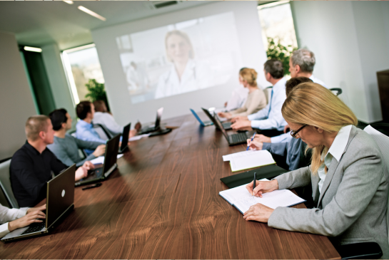 group of people at a meeting table with a presenter on the projection screen