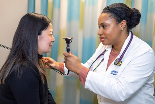 A woman physician in a medical coat examines a woman patient with long, straight har.