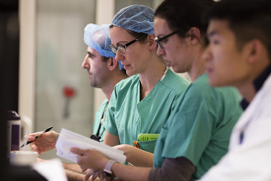 A team of healthcare providers in scrubs reviews patient information at a clinical workstation.
