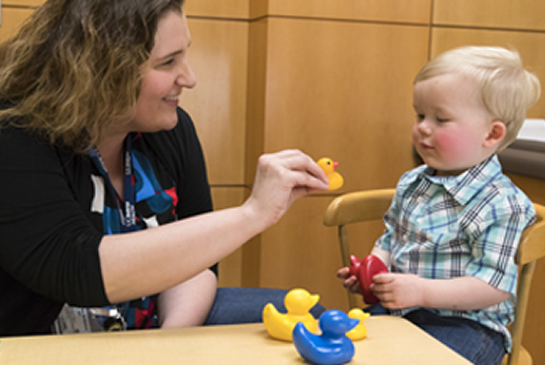 A clinician plays with colorful toys with a toddler during a developmental assessment.