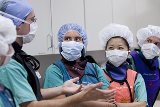 A surgical team in masks and scrub caps confers in an operating room.